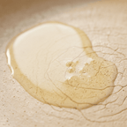 A pool of clear, golden cooking oil sits in the center of a textured, cream-colored non-stick frying pan.